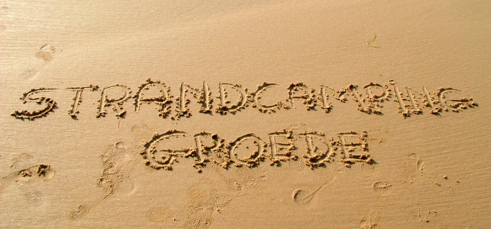 Het woord 'Strandcamping Groede' geschreven in het zand op het strand, omringd door voetstappen – een symbolisch beeld voor duidelijke informatie en eerlijke voorwaarden.