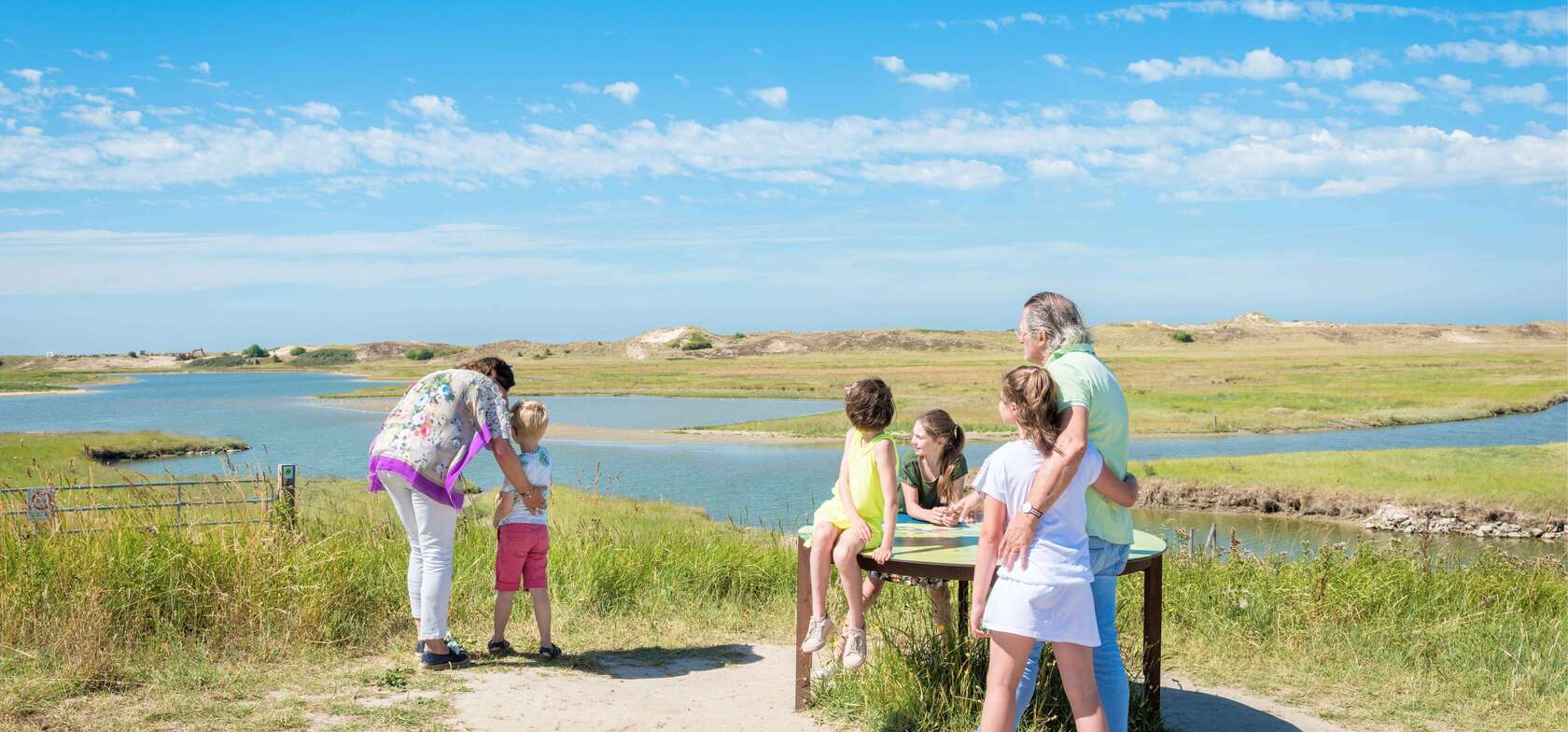 Eine Familie genießt die Natur in der Nähe eines Gewässers – umgeben von grünen Wiesen, sanften Hügeln und einem klaren Himmel. Ideal für gemeinsame Entdeckungen und kulturelle Ausflüge rund um den Strandcamping Groede.