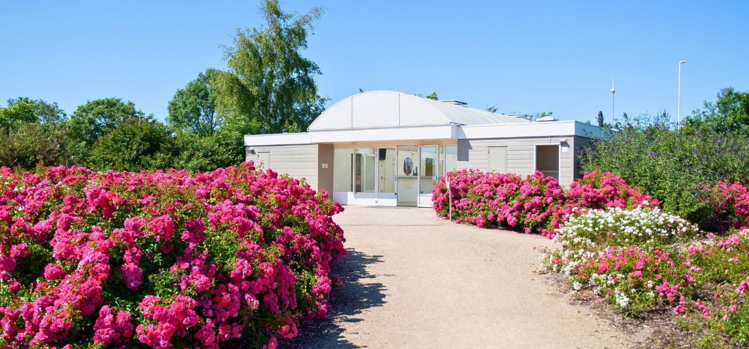 Modernes Sanitärgebäude in gepflegter Gartenanlage mit Blumen und barrierefreiem Zugang.