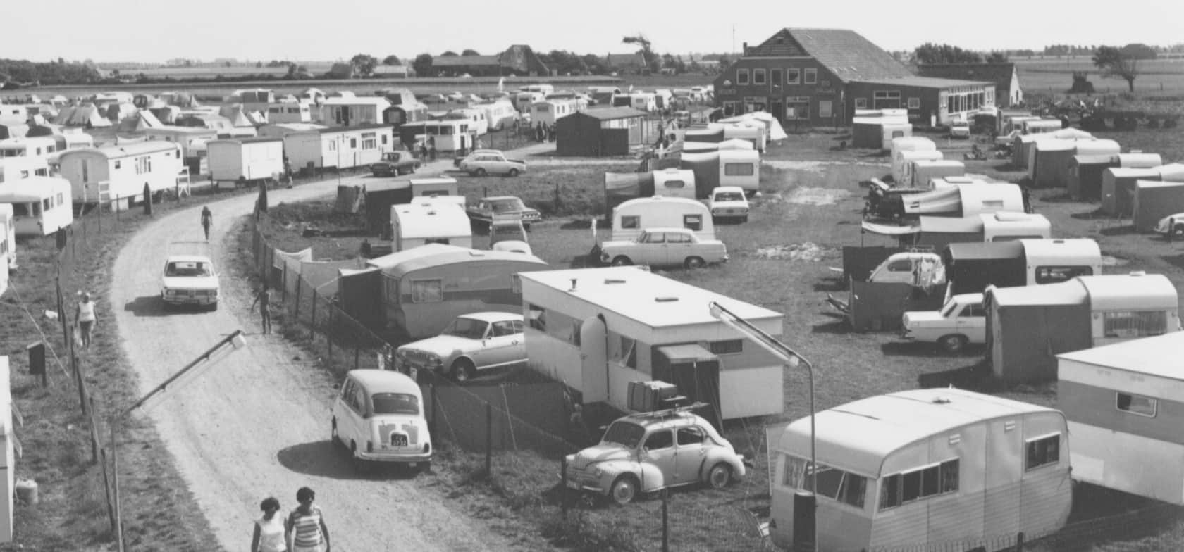 Zwart-witfoto van de vroegere camping met caravans, auto's en een gebouw op de achtergrond – een blik op de geschiedenis van Strandcamping Groede.